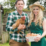 A man and woman hold a chicken in their yard