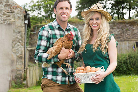 A man and woman hold a chicken in their yard